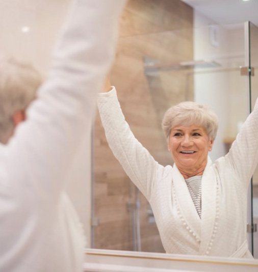 Senior woman joyfully checking out her dental implants in bathroom mirrort